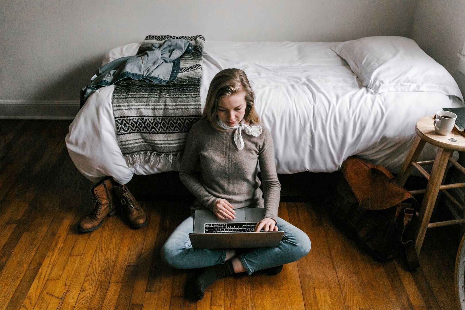 Student sitter på golvet med laptop i en möblerad lägenhet