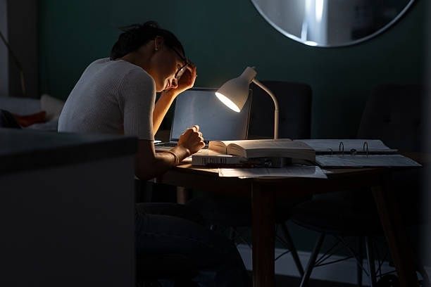 Student sitter vid skrivbord och studerar i skenet från en skrivbordslampa