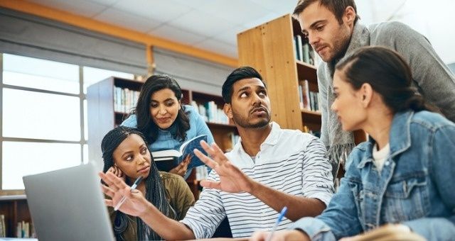Studenter diskuterar ett grupparbete runt en laptop i biblioteket